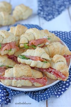 a white plate topped with sandwiches on top of a blue and white table cloth next to rolls