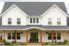 a white house with green front door and two large windows on the side of it