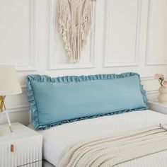 a bed with blue sheets and pillows in a bedroom next to a white nightstand table