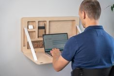 a man sitting in front of a laptop computer on top of a wooden desk shelf