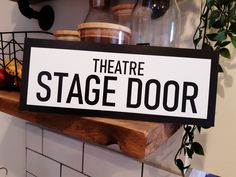 there is a sign that says theatre stage door on the shelf next to some potted plants