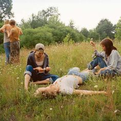 three people are sitting in the grass and one person is laying on the ground while two others stand nearby