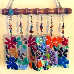 three colorful glass tiles hanging from a wooden rack with beads and chains attached to them