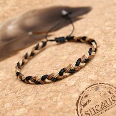 a brown and black braided bracelet sitting on top of a wooden table next to a feather