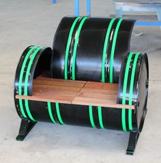 a bench made out of two large black barrels with green stripes on the bottom and sides