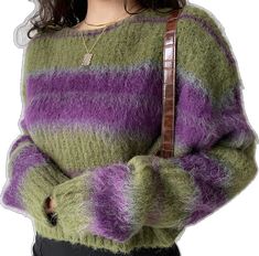 a woman wearing a green and purple sweater with her hands in her pockets while holding a brown bag