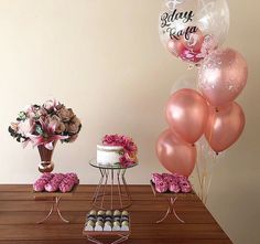 a table topped with lots of pink balloons and flowers next to a cake on top of a wooden table