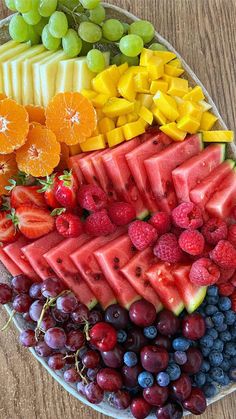 a platter filled with different types of fruit on top of a wooden table next to grapes, watermelon, oranges and raspberries