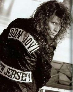 a black and white photo of a woman with long hair wearing a leather jacket that says born to rock new jersey