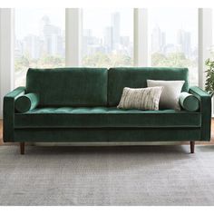 a green velvet couch with two pillows on it in front of a window and a potted plant