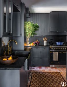 a kitchen with gray cabinets and black counter tops, gold faucets and an area rug