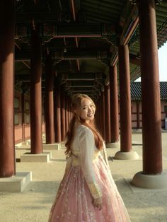 a woman in a pink and white dress is standing under some pillars