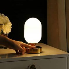 a person reaching for a light on top of a dresser next to a vase with flowers