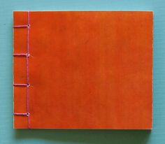 an orange notebook with pink stitching on the front and bottom cover, sitting on a blue surface