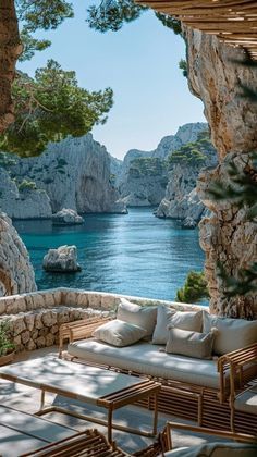 an outdoor seating area overlooks the water and rocky cliffs, which are dotted with white cushions