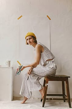 a woman sitting on top of a wooden stool next to a white wall holding an umbrella