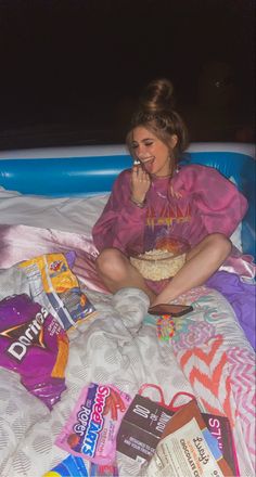 a woman sitting on top of a bed next to bags of food and snacks in her mouth