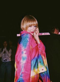 a woman is talking on her cell phone while wearing a tie dye jacket and jeans