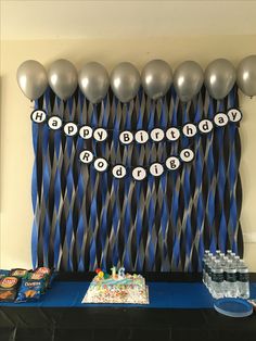 a birthday party with balloons, cake and decorations on a table in front of a blue backdrop