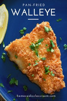 a piece of fried walleye on a blue plate next to lemon wedges and parsley