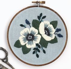 an embroidery project with white flowers and green leaves on a blue background next to scissors