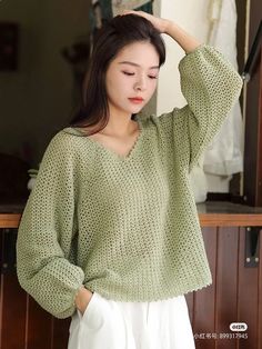 a woman wearing a green sweater standing next to a wooden wall and looking at her hair