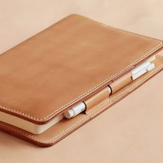 a brown leather notebook with two pens sticking out of the front cover, sitting on a table