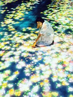 a woman kneeling down on the ground in front of water with flowers all over it