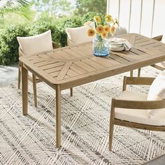 a wooden table sitting on top of a rug next to a white chair and vase filled with flowers