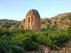 an old tower in the middle of some bushes and trees with mountains in the background