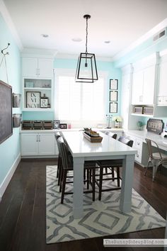 a kitchen with blue walls and white cabinets, an island in the center is surrounded by black chairs