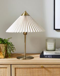 a white lamp sitting on top of a wooden table next to a book and potted plant