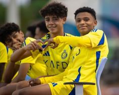 three young men sitting on top of chairs wearing yellow uniforms and smiling at the camera