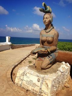 a statue sitting on top of a cement slab next to the ocean with a sky background