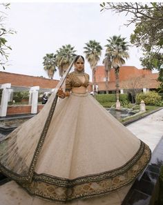 a woman in a white and gold bridal gown standing on the ground with palm trees behind her