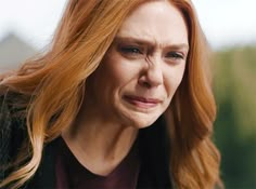 a woman with long red hair is looking at the camera and has an angry look on her face