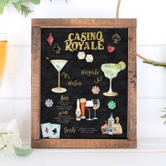 a blackboard with some drinks on it and casino royale written in gold lettering, surrounded by greenery