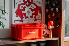 a red box sitting on top of a wooden shelf in front of a wall with pictures