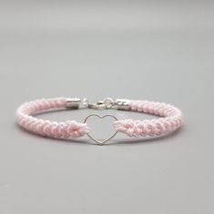 a pink and white bracelet with a silver heart on the clasp, sitting on a gray surface