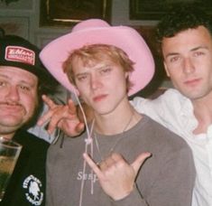 three men posing for a photo with one pointing at the camera and wearing pink hats