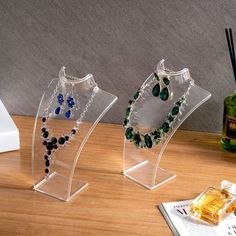 three clear acrylic jewelry stands on a wooden table next to a bottle of perfume