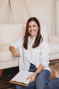 a woman sitting on the floor with a book in her lap and smiling at the camera