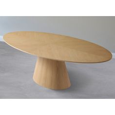 an oval wooden table sitting on top of a cement floor next to a white wall