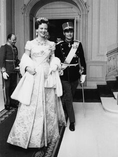 a man in uniform standing next to a woman in a gown and tiara on