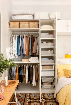 an organized closet with clothes, baskets and other items on shelves next to a bed