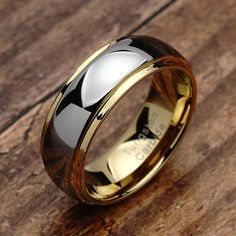 a gold and black wedding ring on top of a wooden table with wood inlays