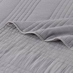 an unmade bed with grey sheets and pillows