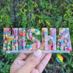 a person holding up the letters that spell out ashshiya in front of some bushes