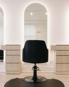 a black chair sitting on top of a hard wood floor in front of two mirrors