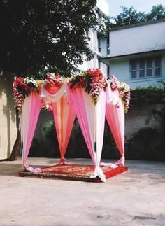 an outdoor wedding setup with pink and white draping, flowers and greenery